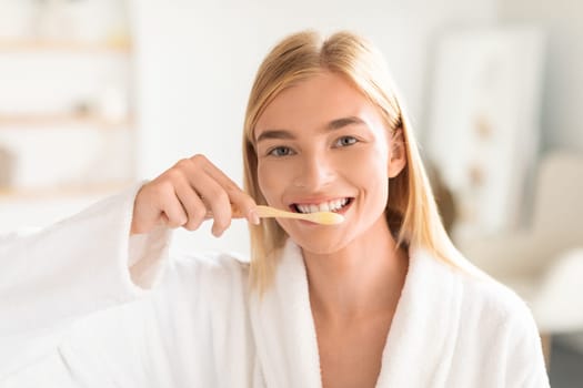 lady in bathrobe brushes teeth with tooth brush in bathroom