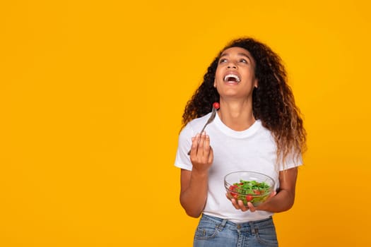 Black lady poses with a healthy green salad meal, studio