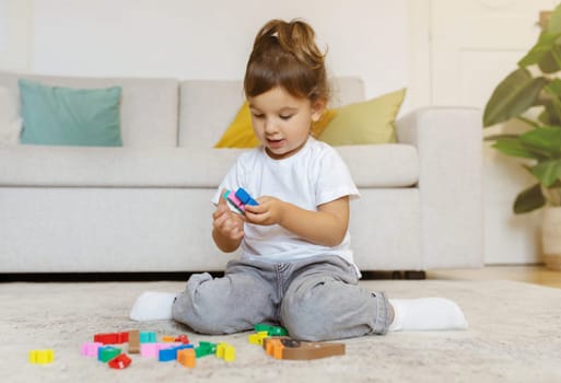 Toddler girl playing with colorful blocks while sitting on floor at home