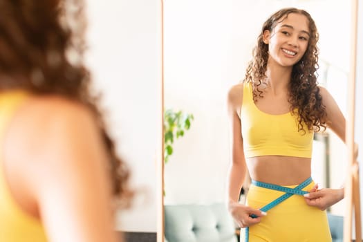 teen girl in sportswear measuring waist with tape at home