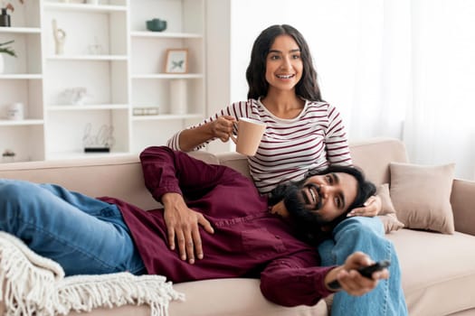 Joyful young indian lovers have fun at home, watching movie