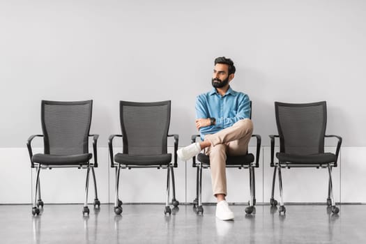 Indian man waiting calmly in a chair, crossed legs, contemplative