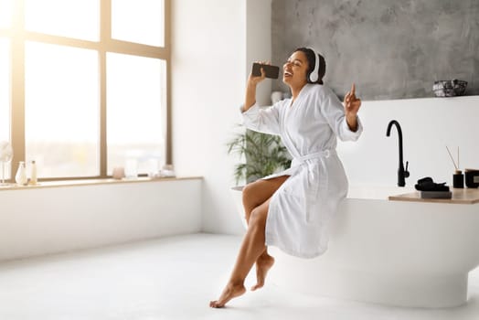 Black woman in white bathrobe singing into her phone as microphone,
