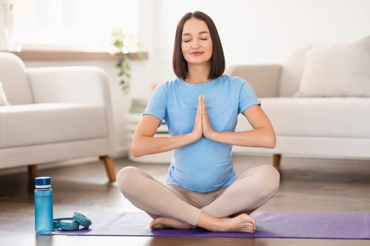 expectant woman sitting in lotus pose on yoga mat indoors
