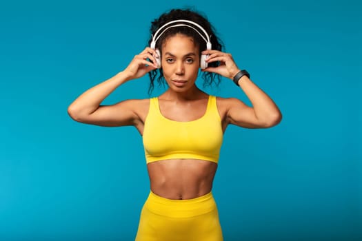 Fit black lady using wireless headphones while training in studio