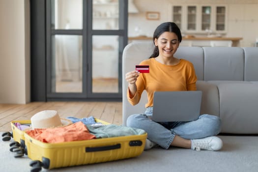 Excited young indian woman using laptop and credit card to book trip