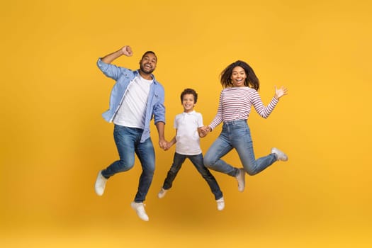 Cheerful Excited African American Family Of Three Holding Hands And Jumping