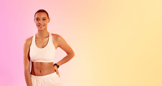 Smiling young fitness enthusiast in a white sports bra and light shorts stands confidently with hands