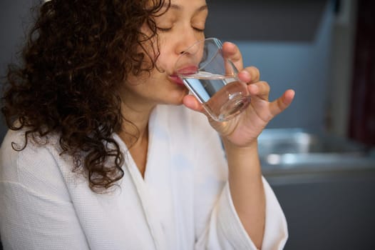 Closeup curly haired pretty woman making sip of water while taking medicine, a painkiller or nutritional supplement