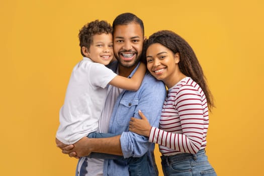 Portrait Of Happy Black Family Of Three With Preteen Son Embracing Together