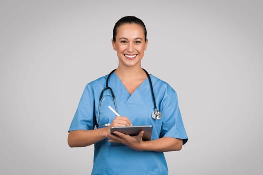 Happy nurse with tablet and stethoscope in scrubs