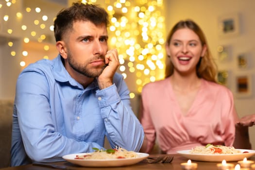 Pensive man at dinner, woman talking in festive setting