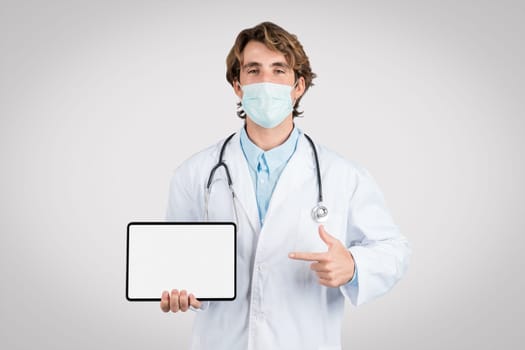 Doctor man in mask showcasing tablet with blank screen