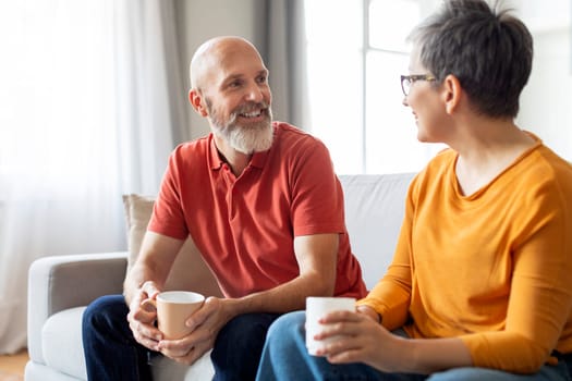 Senior man and woman with coffee in hands enjoying conversation at home
