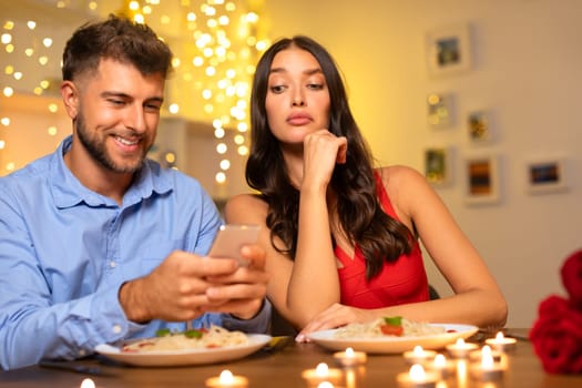 Man engrossed in phone, woman looking bored at dinner