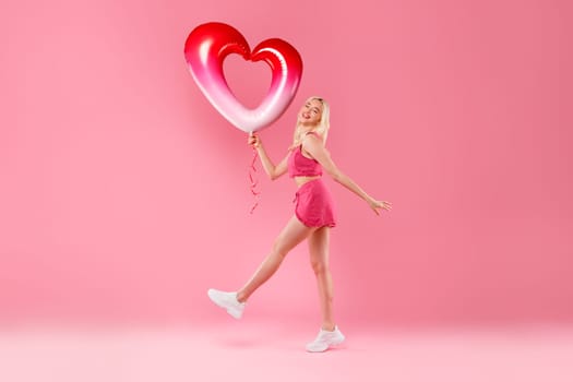 Happy girl dancing with heart balloon in pink
