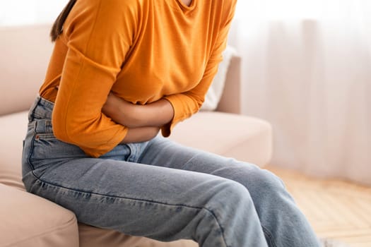 Cropped of woman suffering from stomach-ache, sitting on sofa