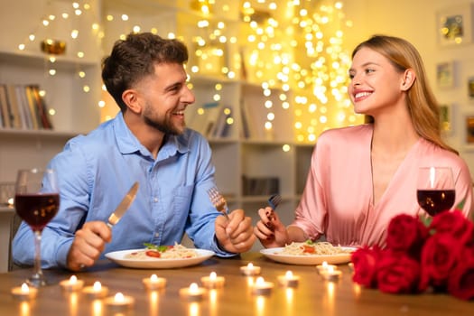 Happy couple enjoying romantic candlelit dinner with wine and pasta