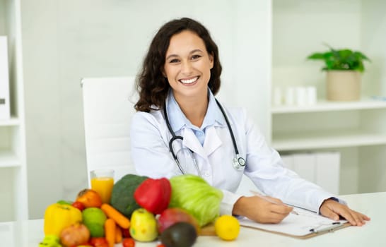 Happy european woman nutritionist sit at desk with fresh fruits