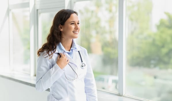 Positive young woman doctor looking through window