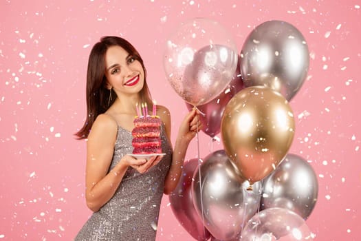 Happy woman with a radiant smile holding a stack of pink-frosted donuts with lit candles