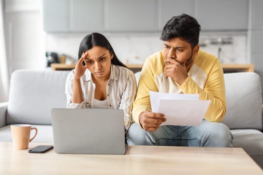 Upset indian couple checking papers and using laptop at home