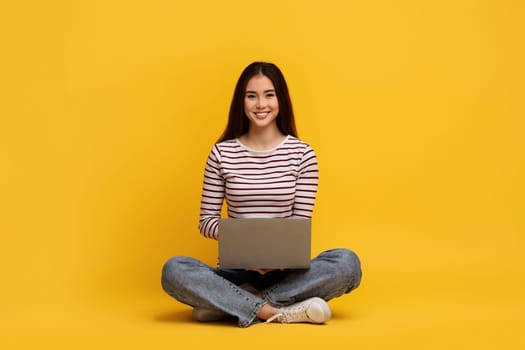Positive young chinese lady student sitting on floor with laptop