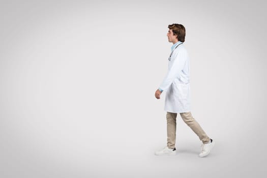 Walking male doctor in lab coat and casual attire, full length, free space