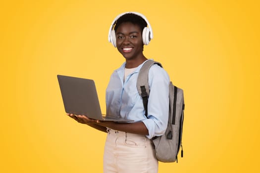 Glad young african american lady student in wireless headphones, use laptop, enjoy online lesson