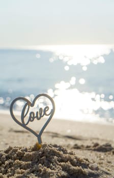 Plastic stick in shape of heart and word Love in sand on beach seashore