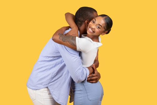 Black woman smiling over shoulder while hugging man on yellow background