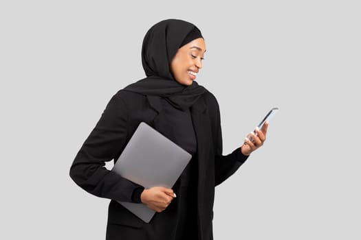 Confident African American businesswoman in a hijab multitasking with a laptop
