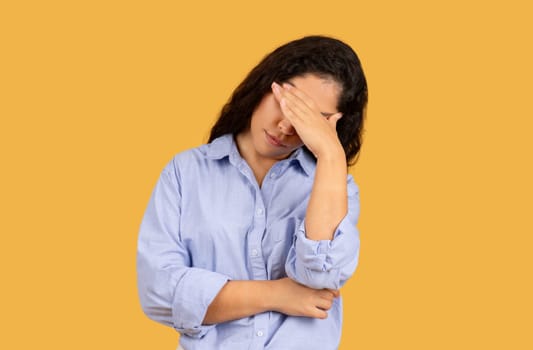 Stressed young woman in a light blue shirt holding her forehead in frustration or headache
