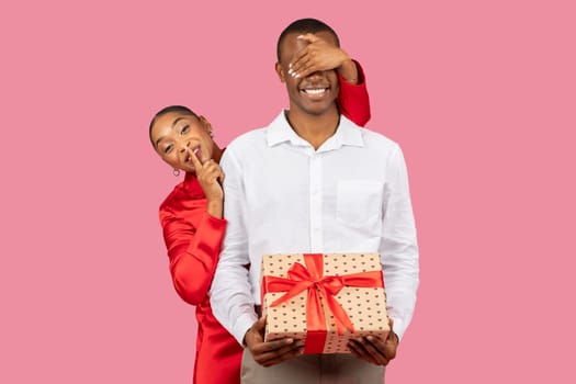 Surprise gift reveal, black woman covering man's eyes, guy holding present