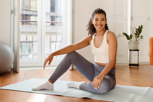 Fit woman in sportswear sitting on yoga mat at home