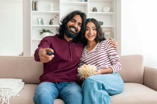 Positive millennial indian man and woman watching TV