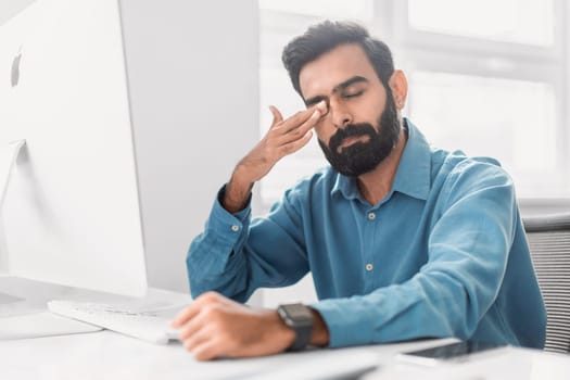 Stressed indian businessman with headache at computer desk