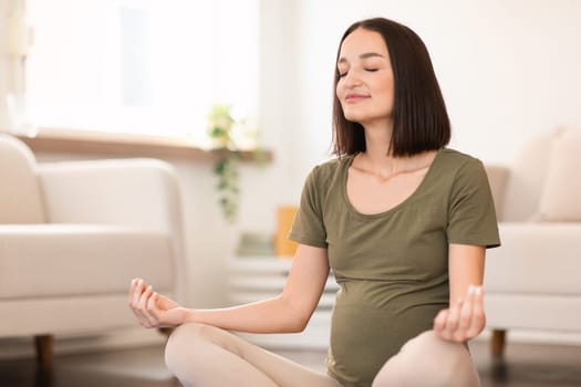 Pregnant lady sits in lotus position in meditation at home