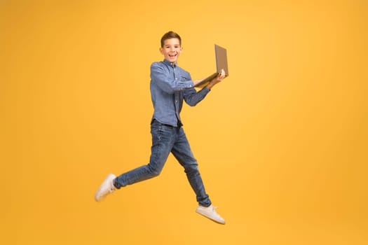Happy teen boy with laptop computer jumping up over yellow background