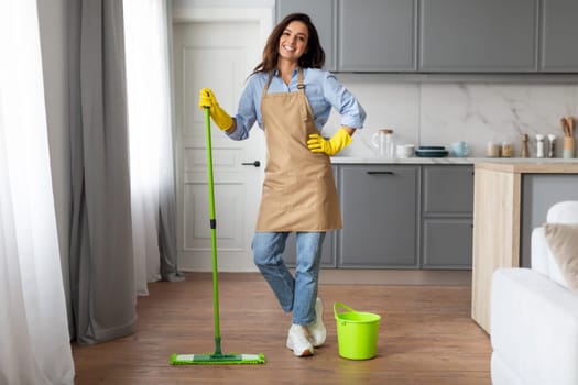 Happy female cleaner posing with mop and bucket in modern kitchen