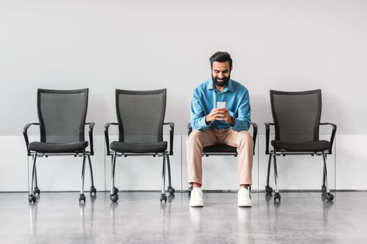 Indian man using smartphone while sitting in empty waiting area