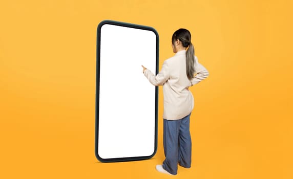 Millennial woman in suit, point finger at big smartphone with blank screen, use gadget