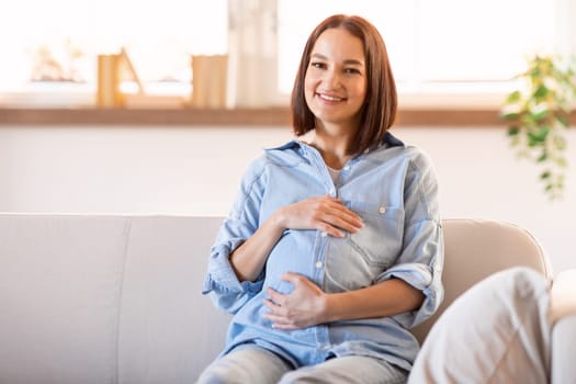 european pregnant woman radiating happiness sits on couch indoor
