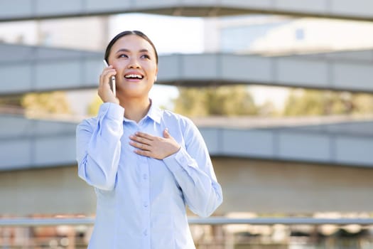 Joyful Japanese businesswoman smiling chatting on her phone, standing outside
