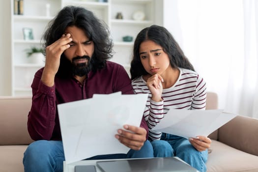 Upset millennial indian spouses checking bills, reading documents