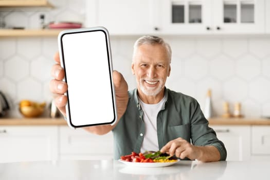 Happy Senior Man Eating Breakfast And Showing Big Blank Smartphone At Camera