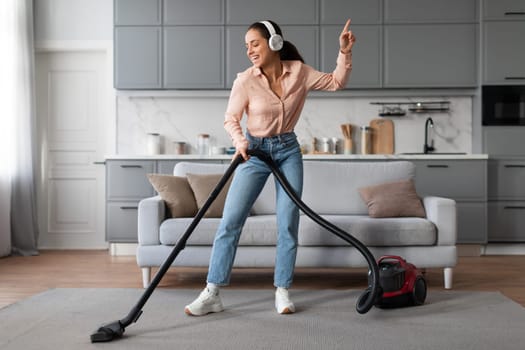Happy woman dancing with vacuum cleaner and headphones