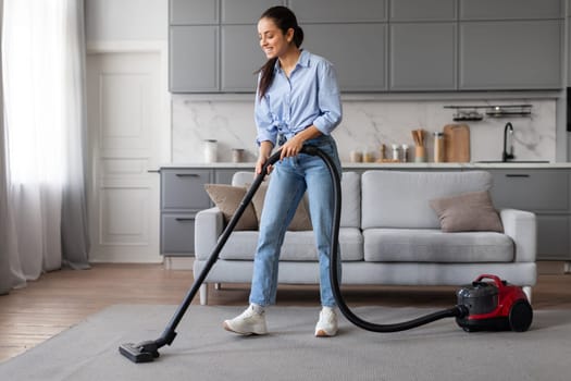 Young woman using vacuum cleaner on carpet in living room