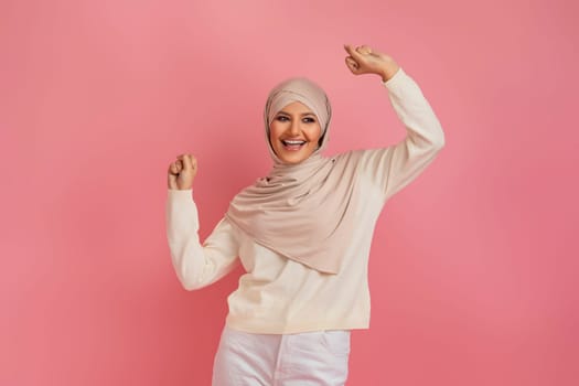 Enthusiastic arab muslim woman in a hijab celebrating success by shaking fists