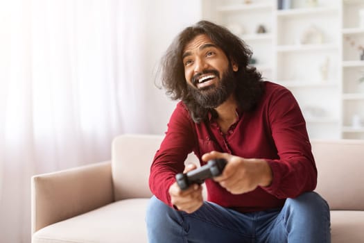 Emotional eastern guy playing video game with joystick at home